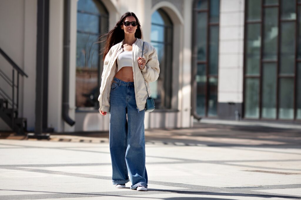 Fashionable woman with long flowing hair wearing trendy white bomber jacket, short Tshirt, wide