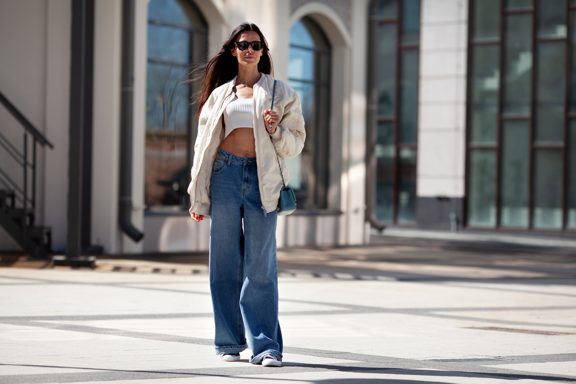 Fashionable woman with long flowing hair wearing trendy white bomber jacket, short Tshirt, wide